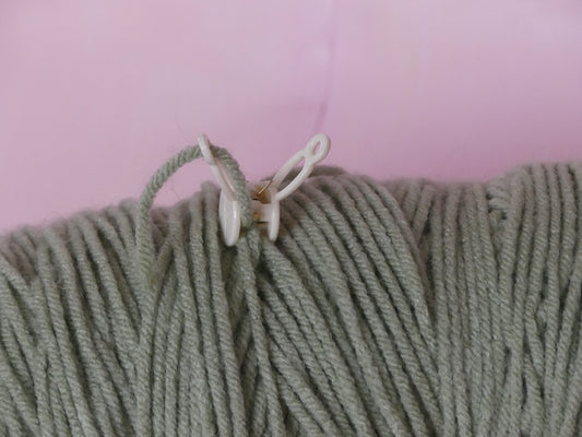 close up of a green yarn skein with its end secured by the Loop Lock yarn organization tool